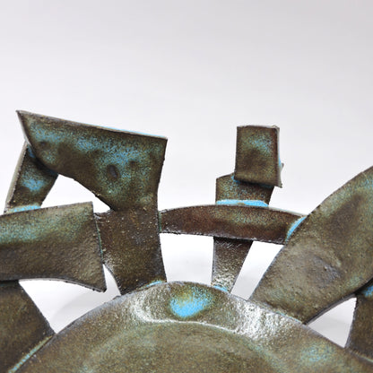 A close-up of the ATLANTIS 'BRUTE' BOWL, an abstract, handmade stoneware piece with geometric forms and a bronze-green patina, displayed against a plain white background.