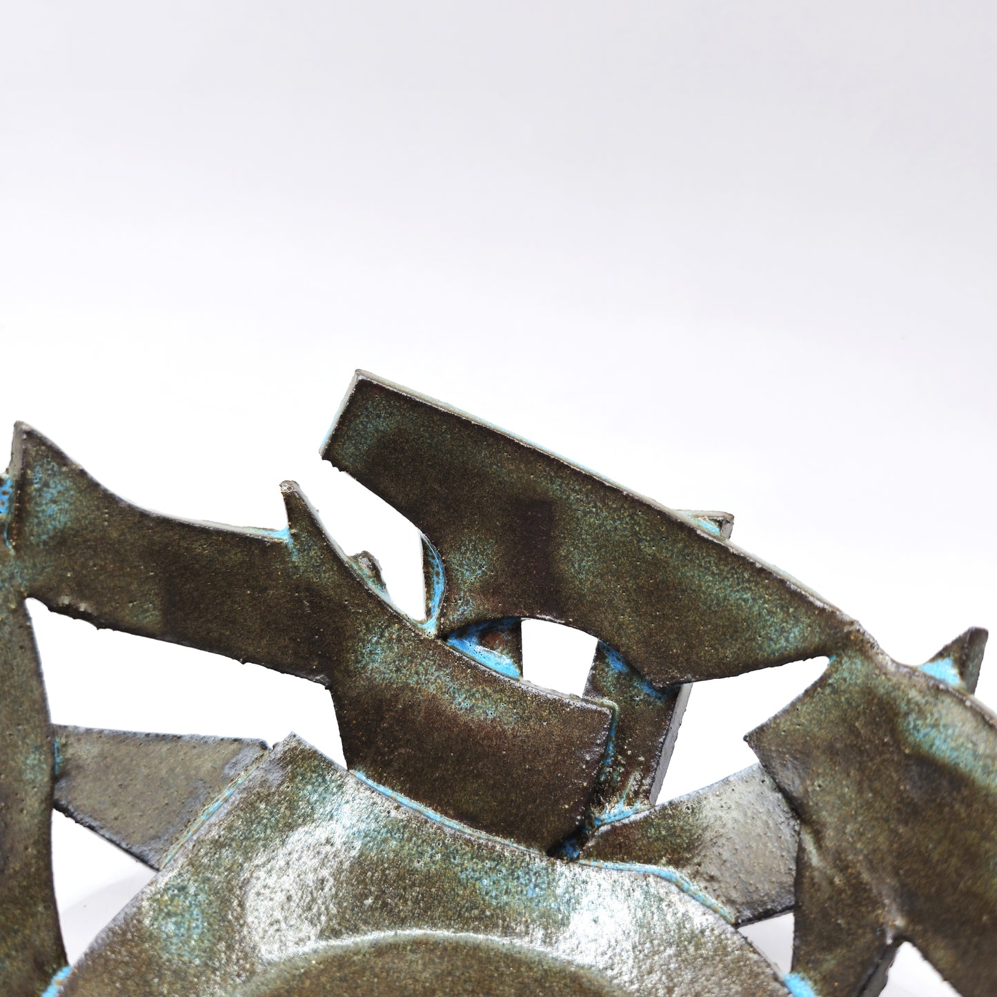 A close-up of the ATLANTIS 'BRUTE' BOWL, a handmade stoneware sculpture with jagged, overlapping edges and a distressed greenish-blue patina, its abstract geometric form set against a plain white background.