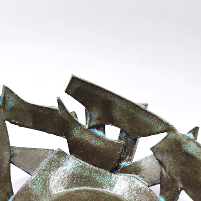 A close-up of the ATLANTIS 'BRUTE' BOWL, a handmade stoneware sculpture with jagged, overlapping edges and a distressed greenish-blue patina, its abstract geometric form set against a plain white background.
