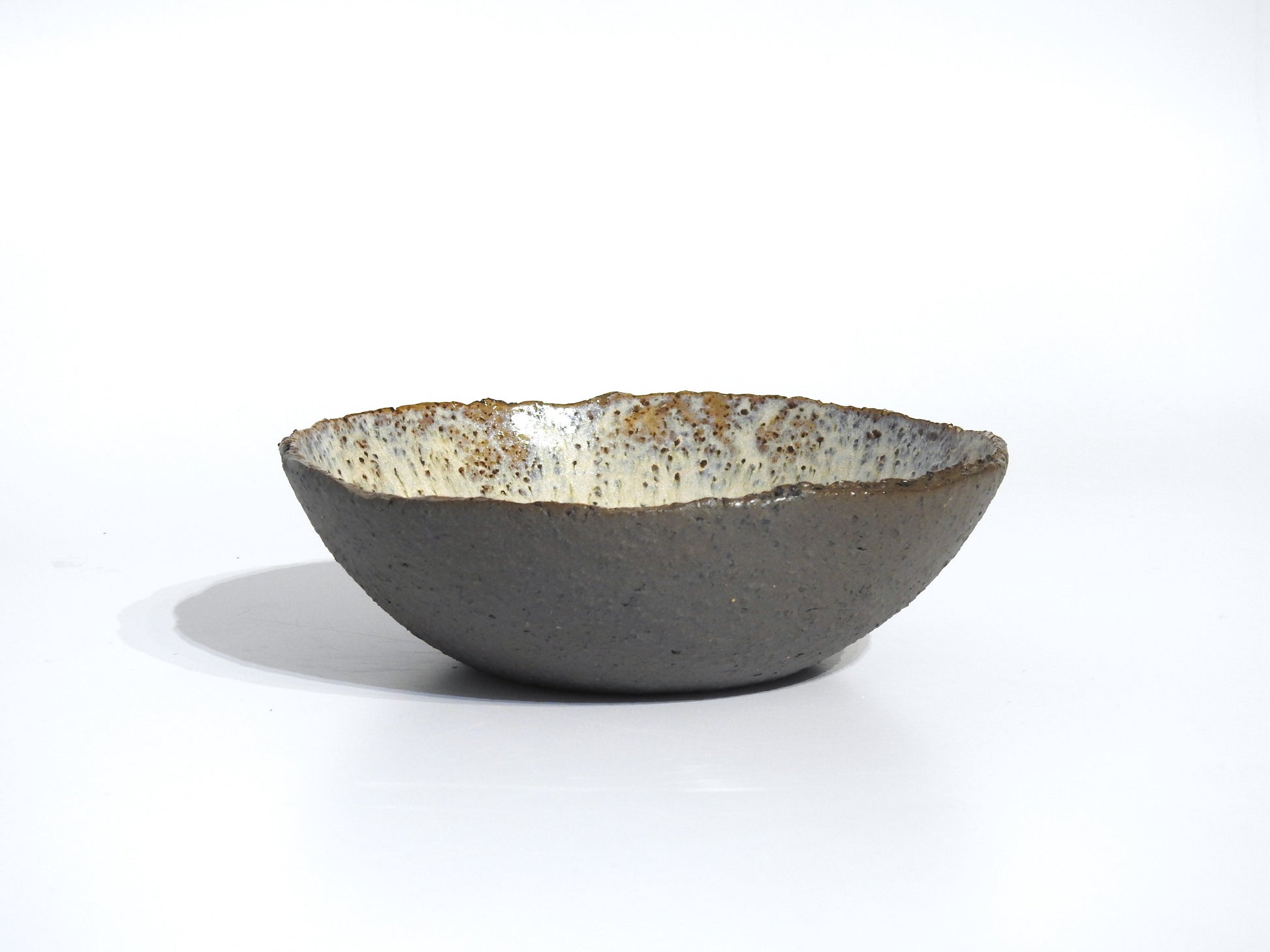 The STONE SOUP BOWL is a handmade ceramic piece featuring a textured brown exterior and a speckled, glazed white interior, ideal for serving meals straight from your small frying pan. Shown on a plain white background.