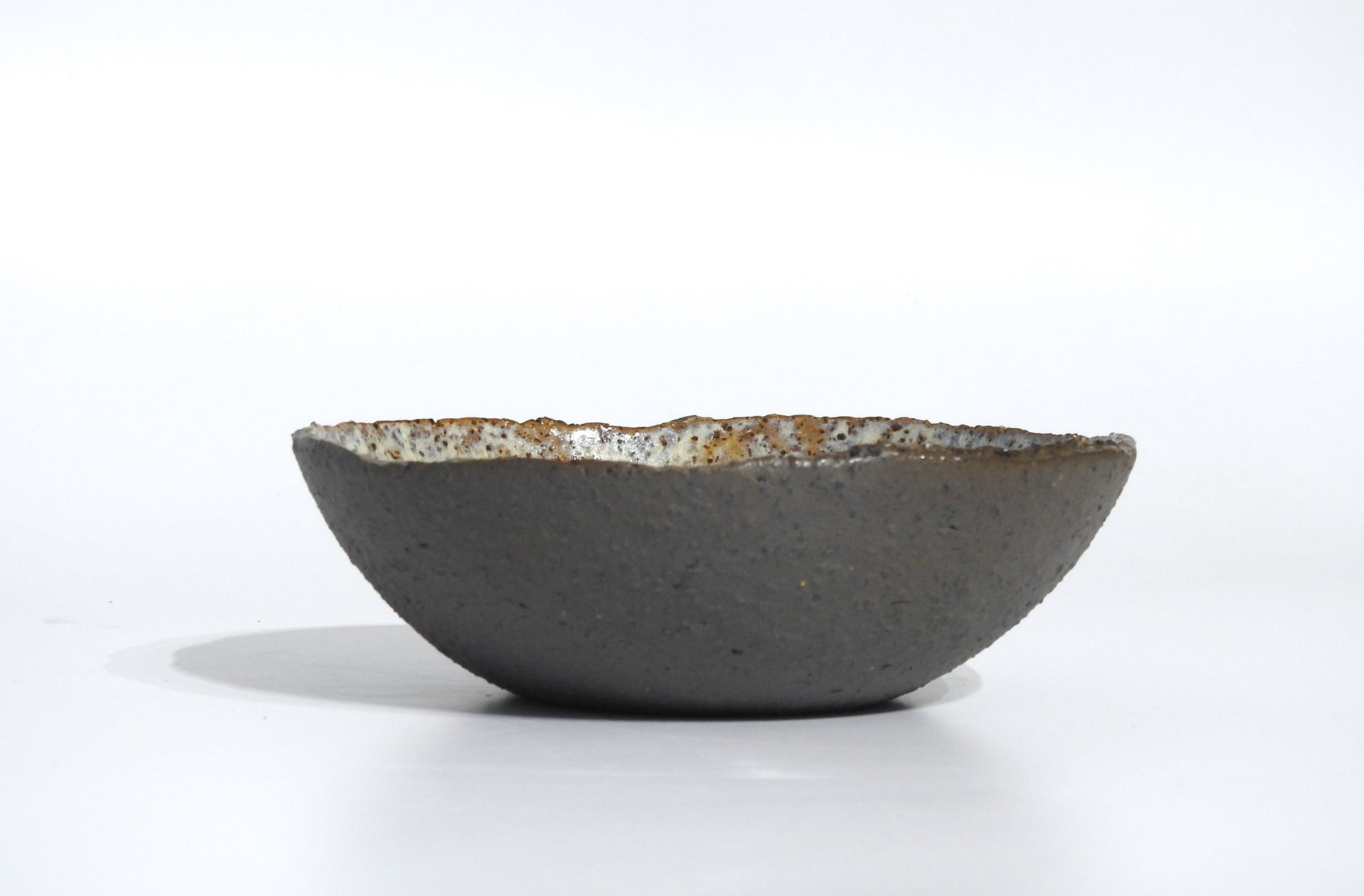 The STONE SOUP BOWL is a handmade, round ceramic bowl with a textured dark gray exterior and slightly uneven rim, measuring 18 cm in diameter, displayed on a white background.