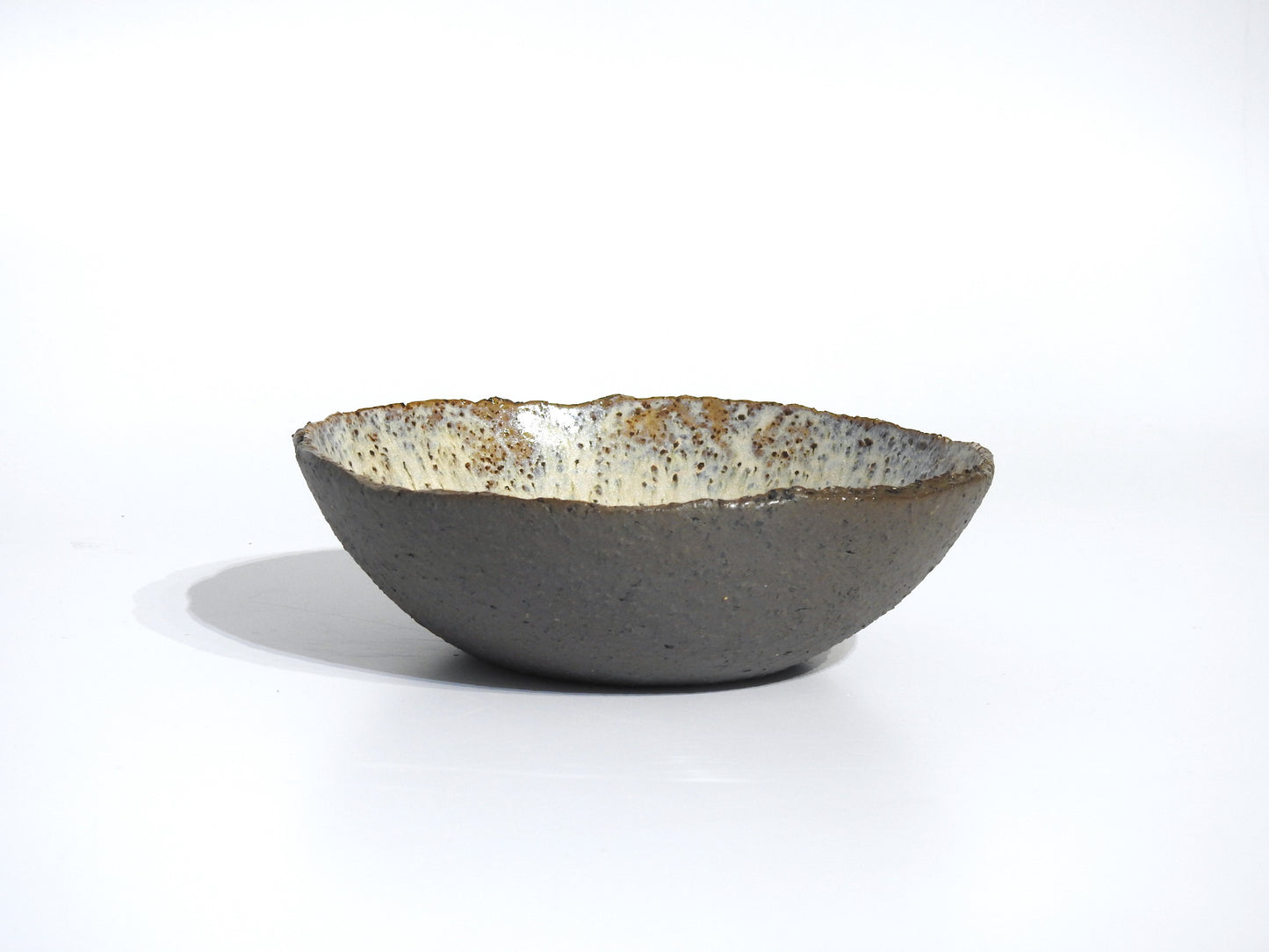 The STONE SOUP BOWL is a handmade 18 cm ceramic piece with a rough, textured gray exterior and a speckled, glossy white interior, shown against a plain white background.