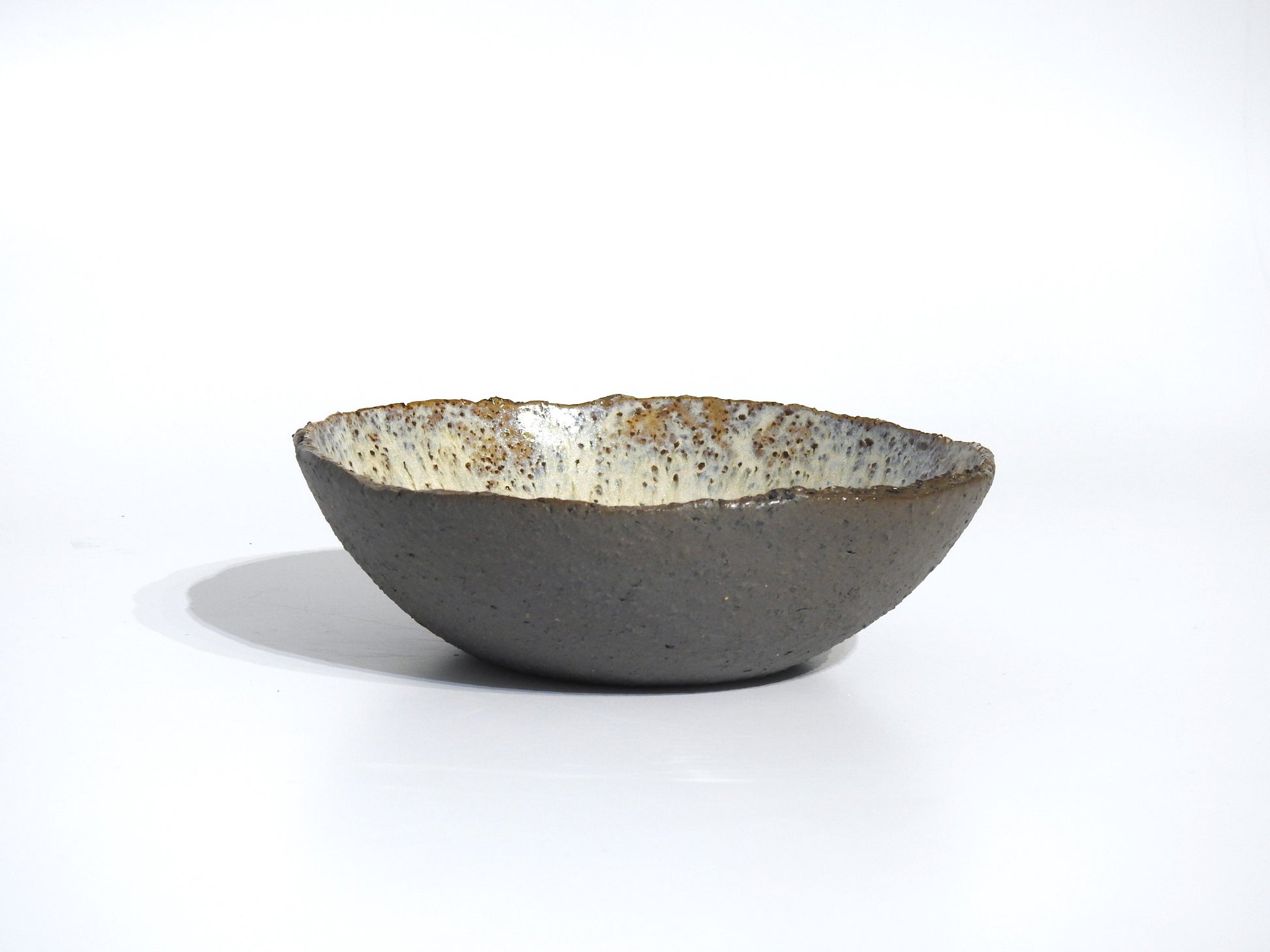 The STONE SOUP BOWL is a handmade 18 cm ceramic piece with a rough, textured gray exterior and a speckled, glossy white interior, shown against a plain white background.