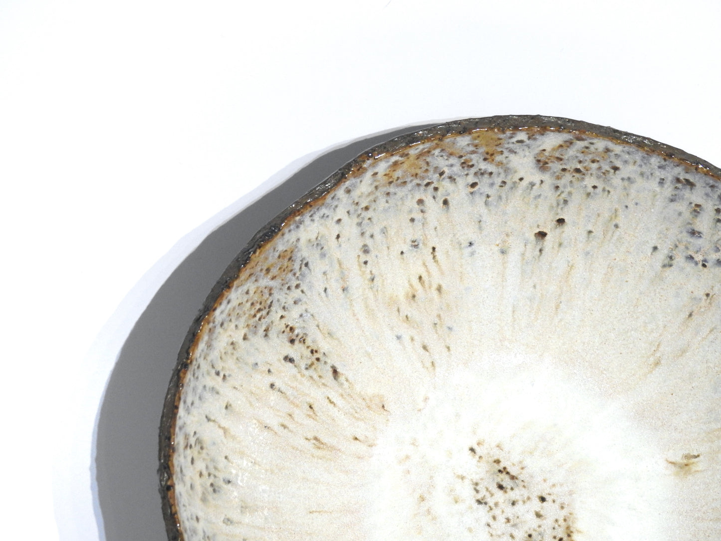 Close-up of the STONE SOUP BOWL—a round, white bowl with slight texture, brown speckles, and a thin dark rim—casting a shadow on a plain white background, partially visible in an 18 cm pan.