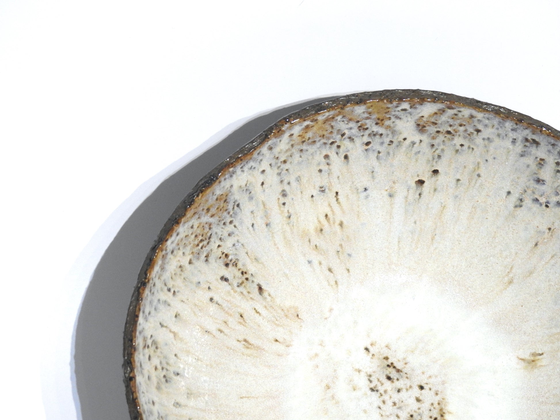 Close-up of the STONE SOUP BOWL—a round, white bowl with slight texture, brown speckles, and a thin dark rim—casting a shadow on a plain white background, partially visible in an 18 cm pan.