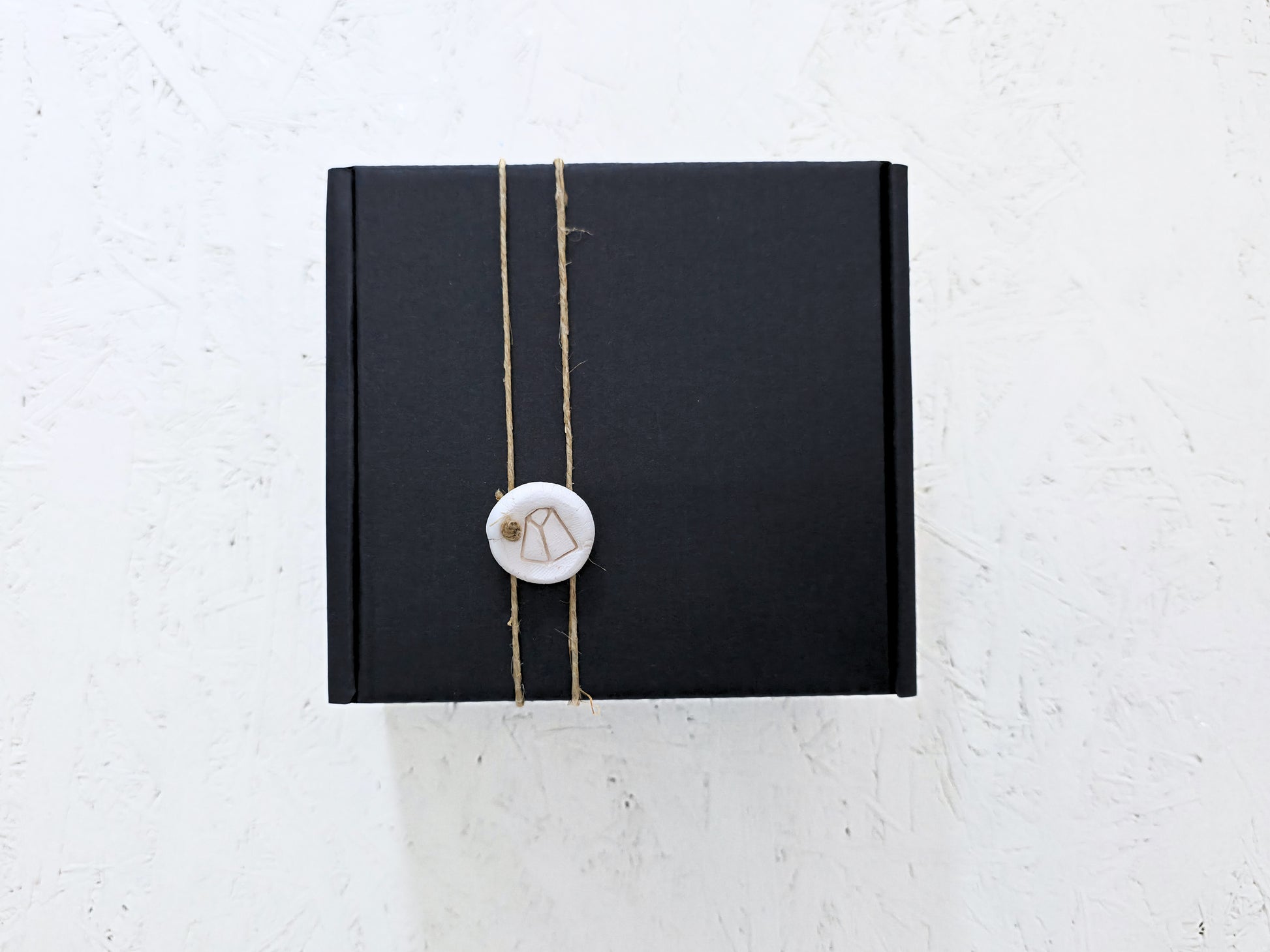 Box 10 by Magma Lab, a luxury gift box tied with twine and sealed with a round white wax stamp, is perfect for Christmas gifting and looks elegant on any textured white surface.