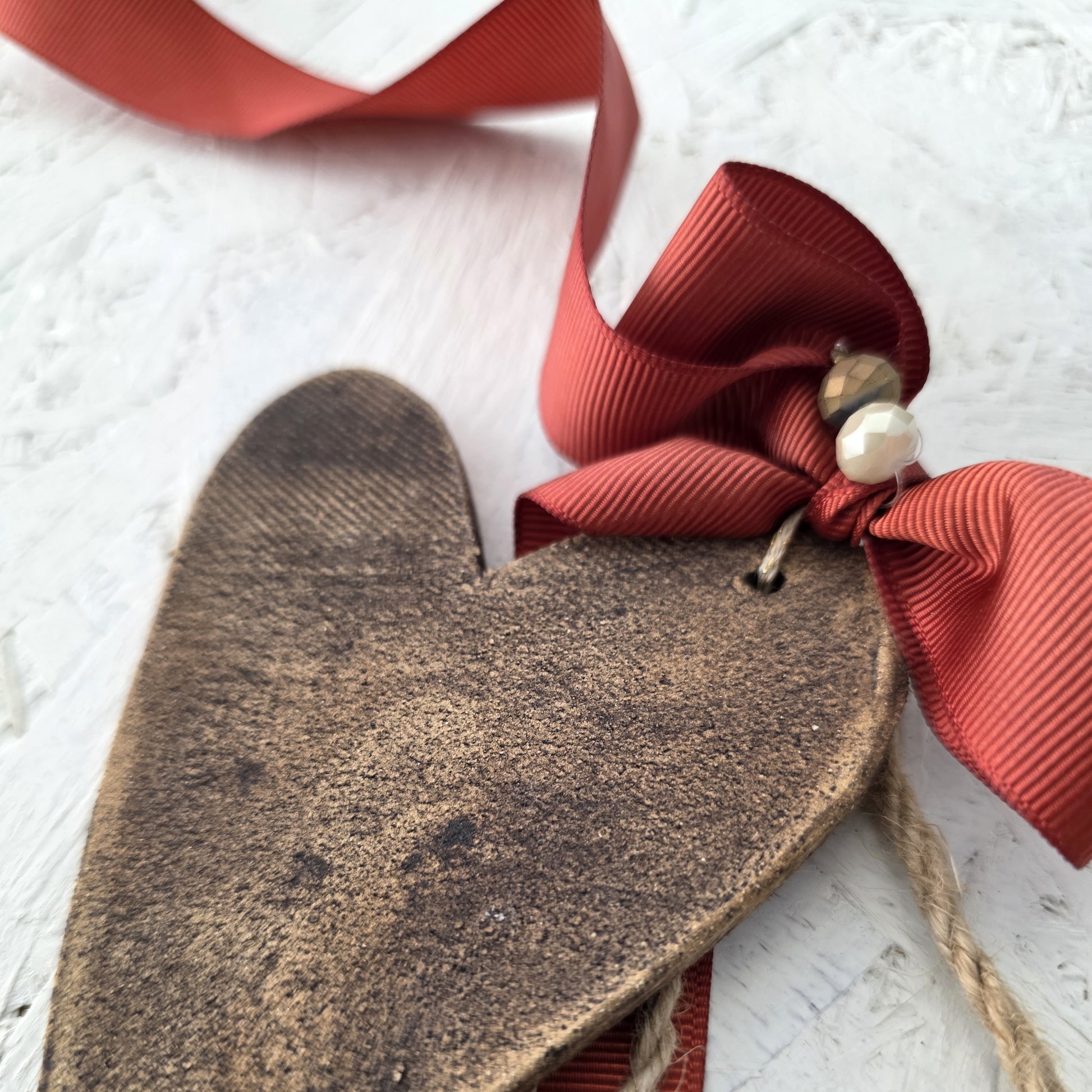 Heart-shaped brown ceramic  tag with a red ribbon and pearl accent on a textured white background