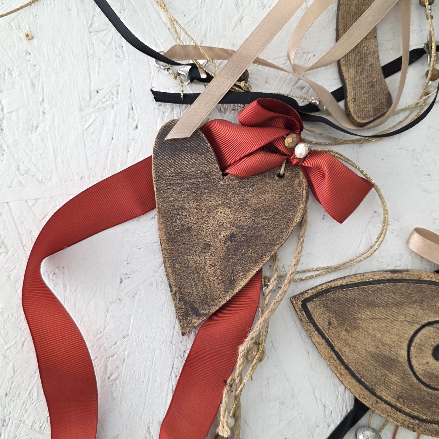Heart-shaped brown ceramic ornament with red ribbon on a textured white surface