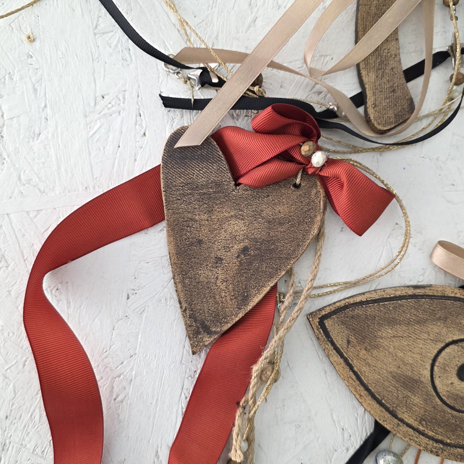 Heart-shaped brown ceramic ornament with red ribbon on a textured white surface