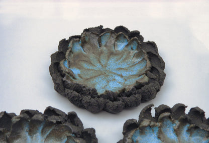 The ATLANTIS ashtray is a handmade ceramic piece with a textured dark brown, petal-shaped rim and blue speckled center. Its uneven, organic edges resemble a flower or lotus, making it an artisanal accent for any surface.