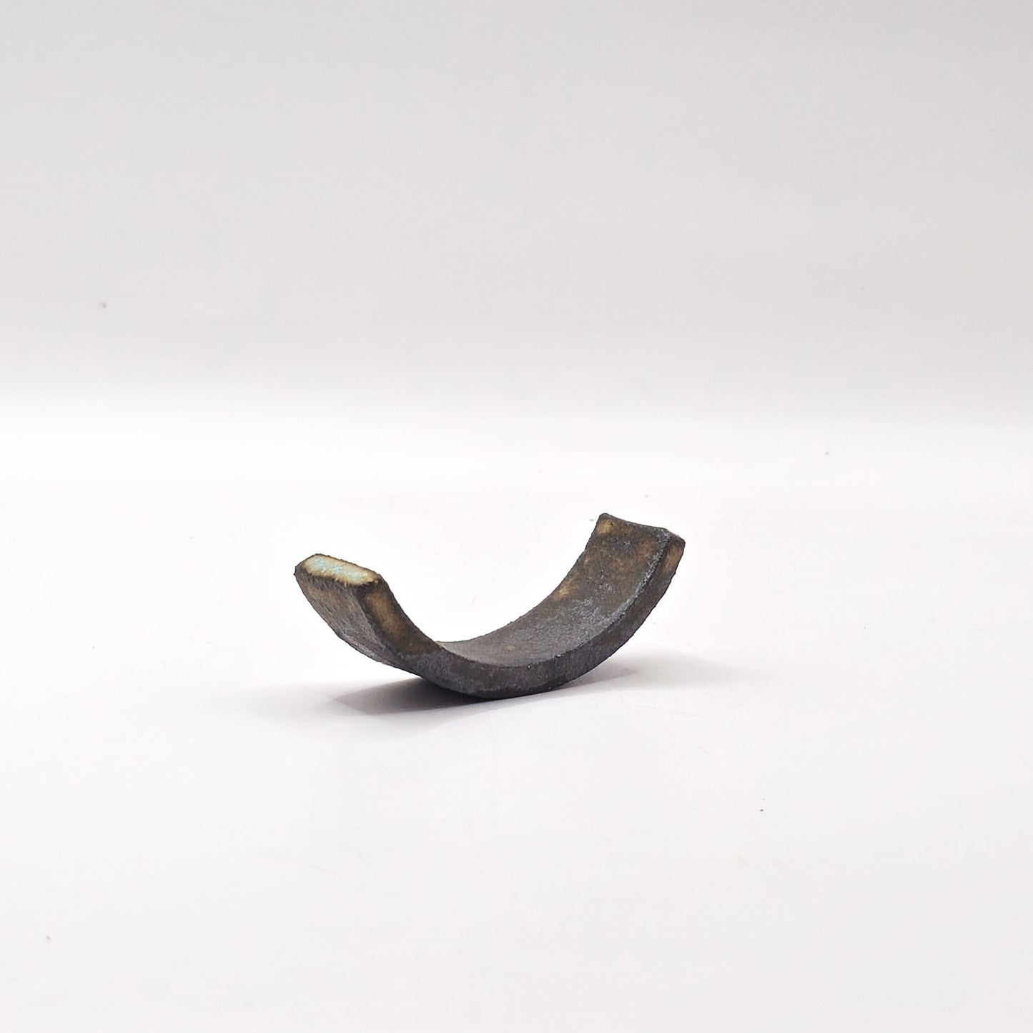 The SOIL CHOPSTICKS REST, a curved metallic piece shaped like a half ring or open bracket, stands upright against a plain white background, evoking the elegance of Greek craftsmanship.