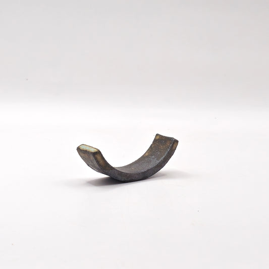 The SOIL CHOPSTICKS REST, a curved metallic piece shaped like a half ring or open bracket, stands upright against a plain white background, evoking the elegance of Greek craftsmanship.