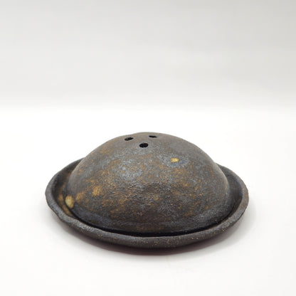 The SOIL INCENSE HOLDER Set features a round, dome-shaped rustic brown incense holder with three top holes, displayed on a matching circular base of handmade stoneware against a plain white background.