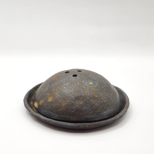 The SOIL INCENSE HOLDER Set features a round, dome-shaped rustic brown incense holder with three top holes, displayed on a matching circular base of handmade stoneware against a plain white background.