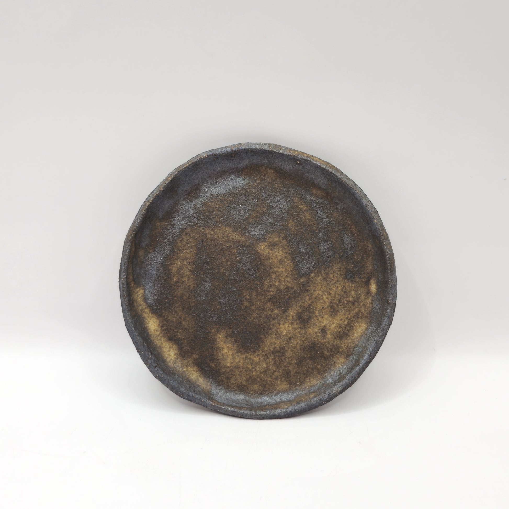 The SOIL INCENSE HOLDER Set features round, rustic ceramic holders with a textured surface in mottled brown and dark gray, showcasing handmade stoneware against a plain white background.