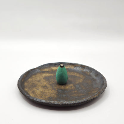 The SOIL INCENSE HOLDER Set features a small, green teardrop-shaped holder with a dark tip on a rustic brown ceramic plate, beautifully showcasing handmade stoneware and Greek craftsmanship against a plain white background.
