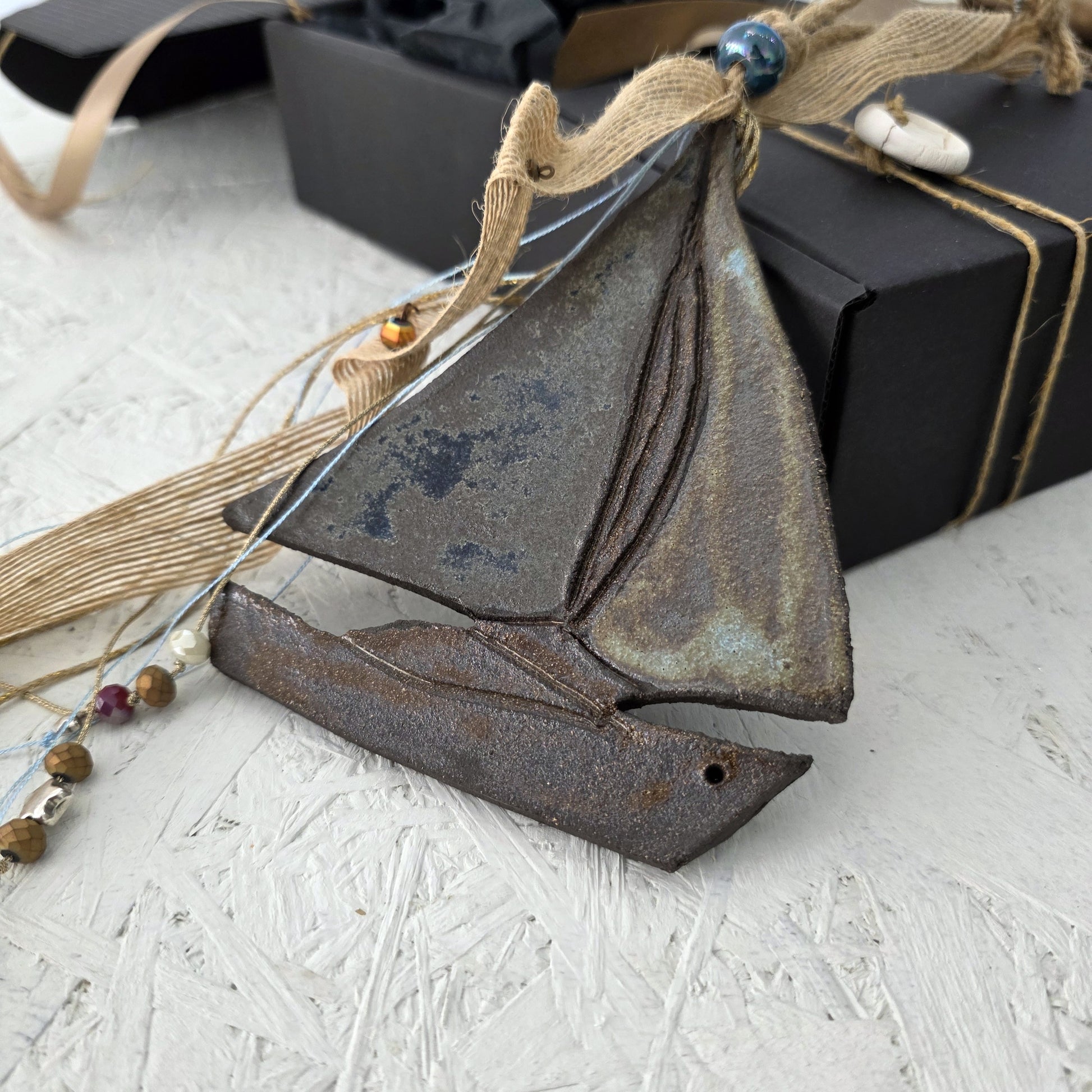 Decorative sailboat ornament on a textured surface with decorative string and beads.